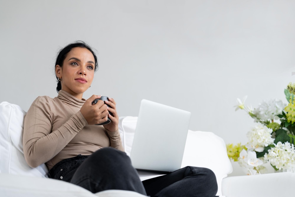 Una mujer feliz tomando café en el sofá de su casa para disfrutar de un momento de terapia