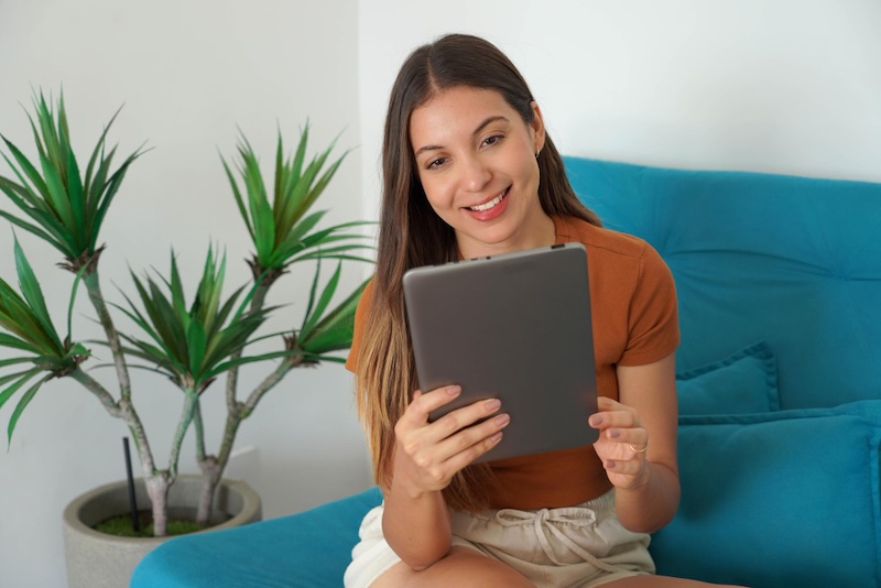 mujer sentada sofá azul con tablet en mano planta detrás