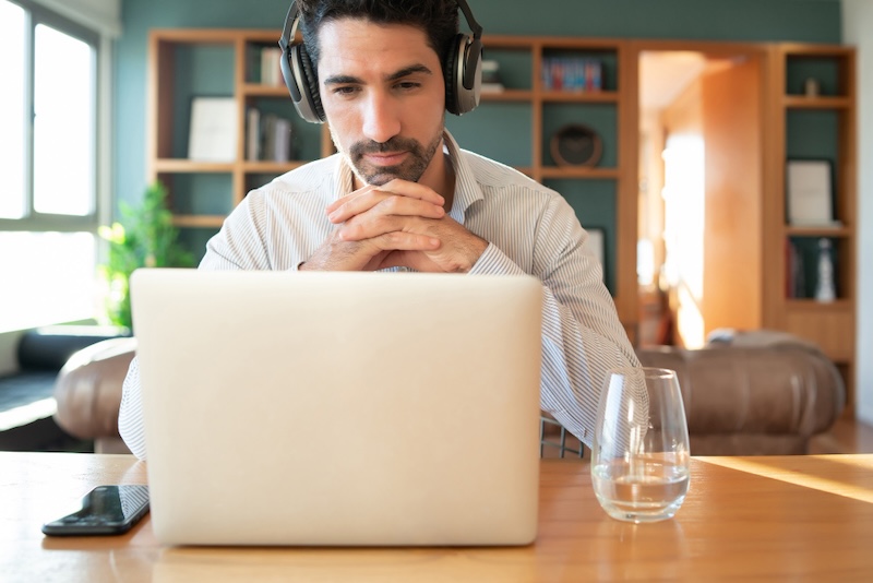 hombre delante de un laptop con auriculares con las manos cruzadas y un vaso de agua