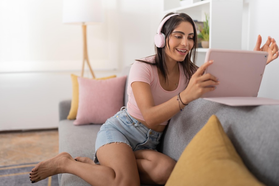 mujer sentada sofá cascos y tablet rosa