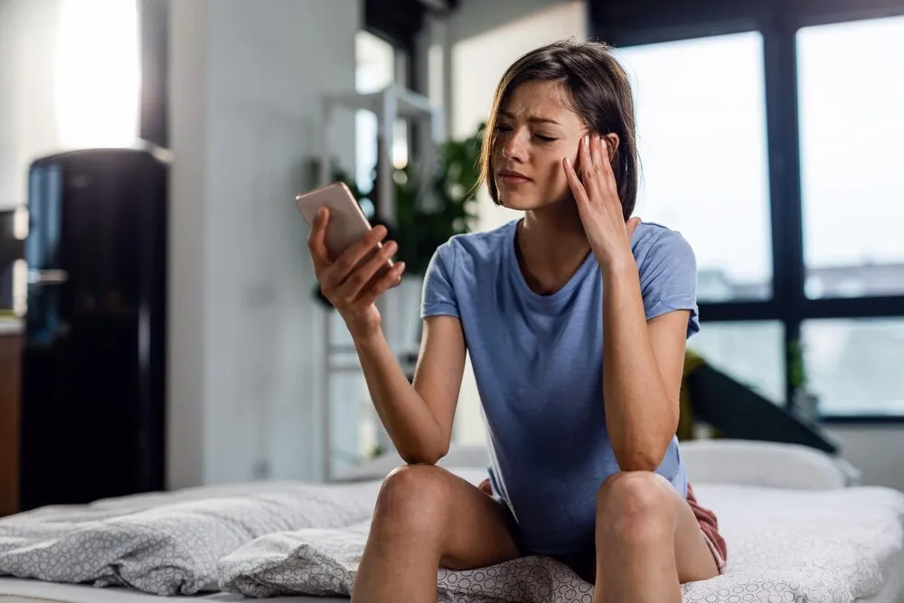 mujer angustiada con dolor de cabeza mientras lee un mensaje que recibió en su celular
