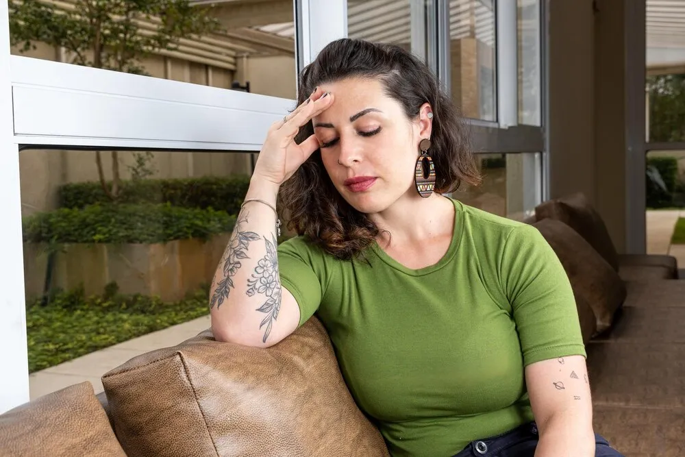brasileño con migraña y tatuado sentado en el sofá café