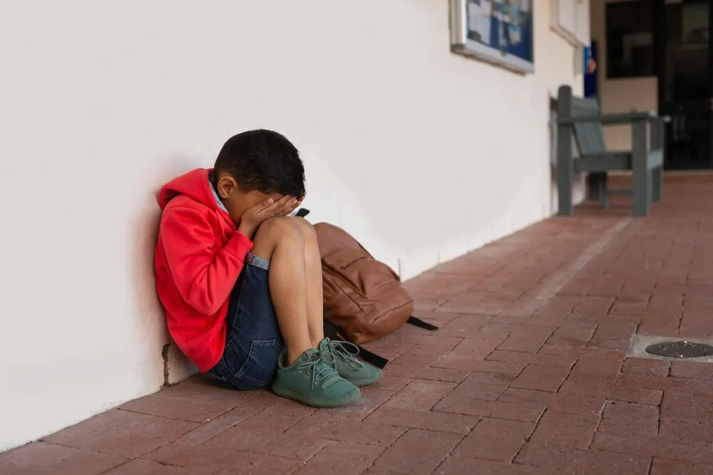 escolar triste sentado solo con las manos cubriéndose la cara en el piso del pasillo