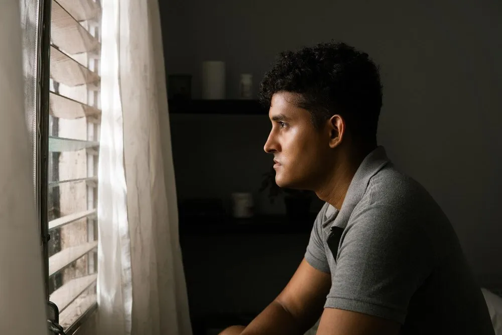 hombre solitario mirando y pensando frente a una ventana concepto de salud mental y crisis masculina