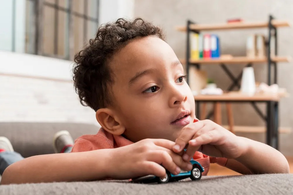 niño negro pensativo jugando con un carrito de juguete