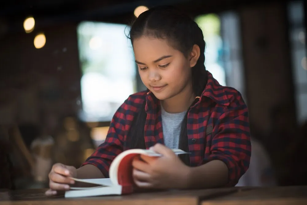 Mujer joven leyendo un libro sentada en el interior de una cafetería urbana.
