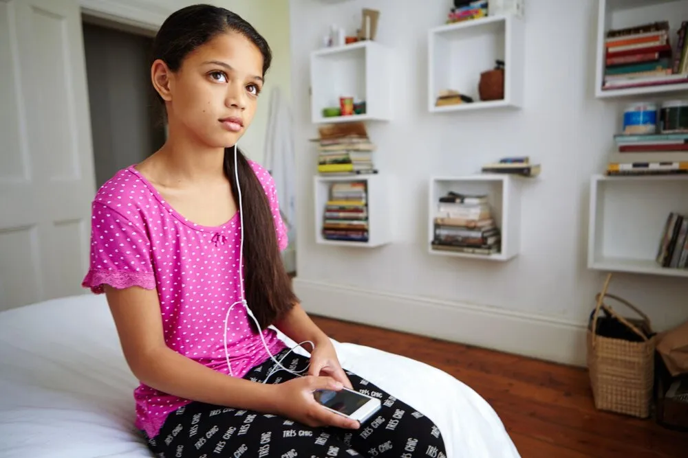 niña pensando y teléfono en la recámara con audífonos para streaming de música, lista de reproducción para niños y entretenimiento, reflexión de la niña y tecnología de audio en la cama con aplicación móvil para álbum de canciones e internet en el hogar.