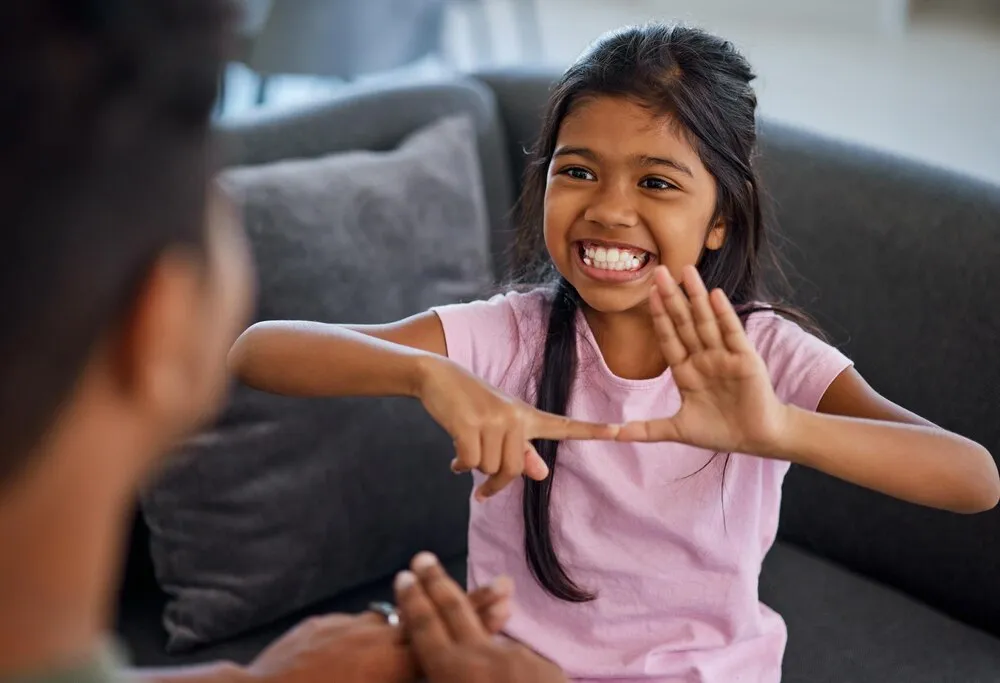 lengua de señas infantil y aprender a comunicarse con una niña o padre sordos mientras hace señas con los dedos y muestra símbolos visuales en casa, niño feliz con discapacidad auditiva o pérdida de audición sentado con un tutor