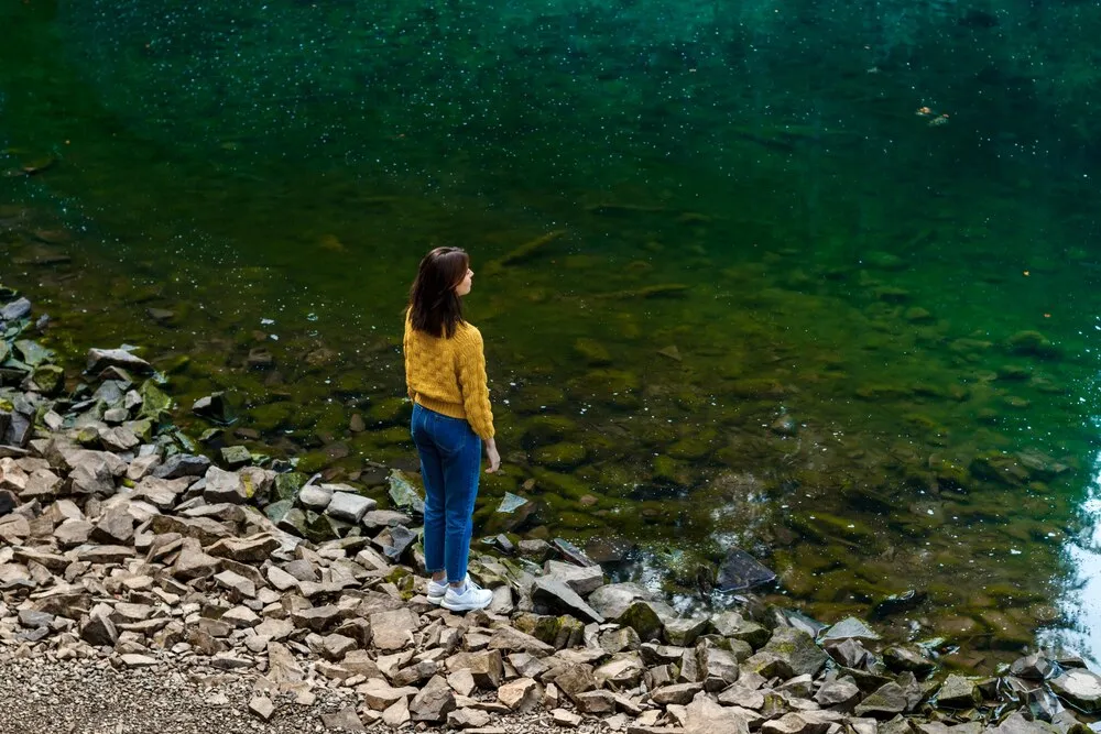 Hermosa mujer morena disfrutando el paisaje de las montañas, parada cerca de un lago.