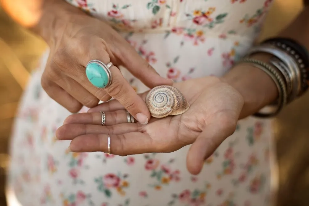persona sosteniendo caracola en mano anillos pulseras esmeralda verde